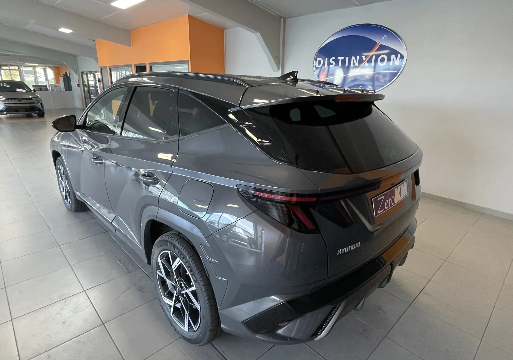 Vue 3/4 arrière droite d'un Hyundai Tucson 2025 gris Ecotronic, avec jantes sport et vitres teintées en showroom.