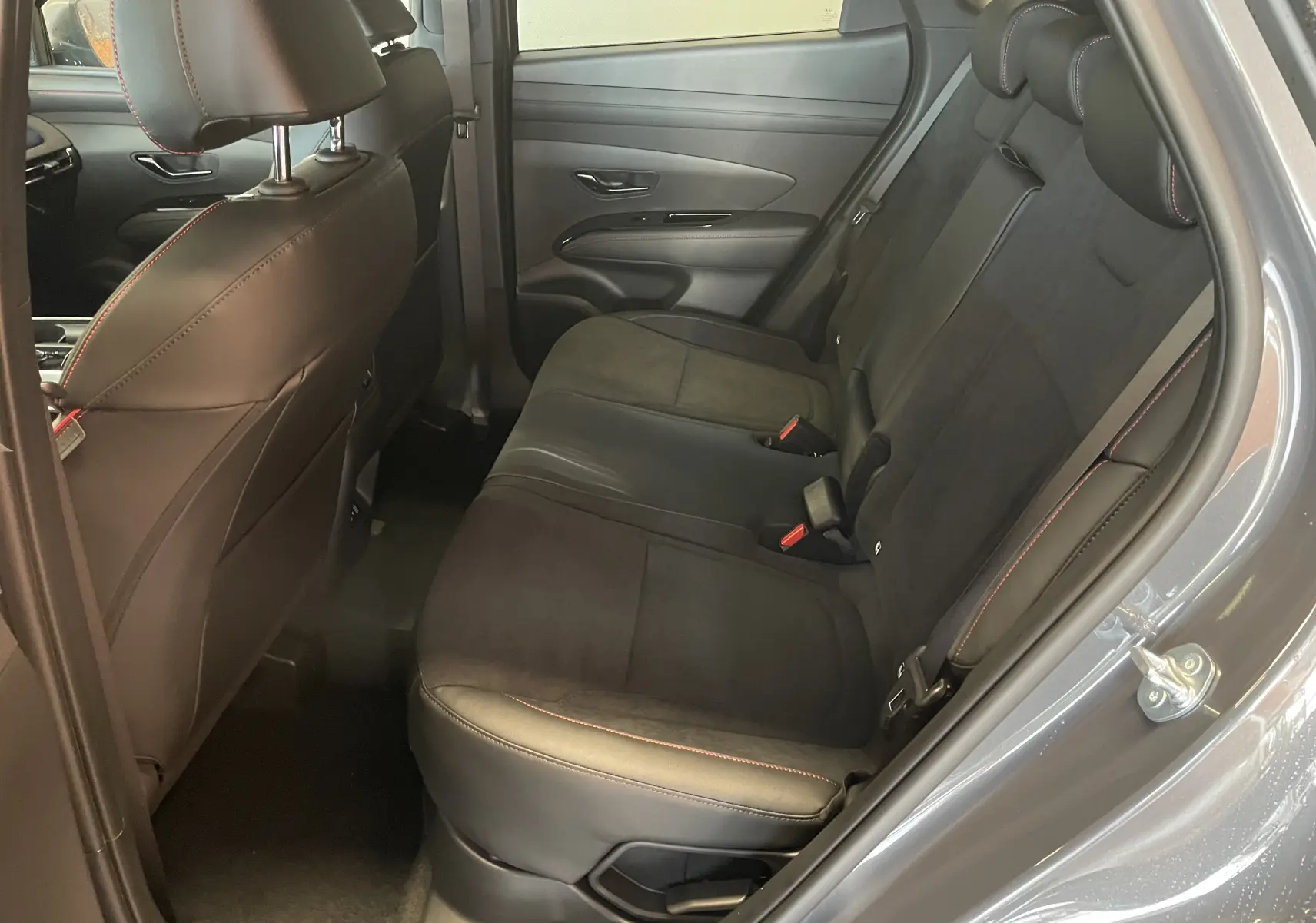 Vue côté droit de l'habitacle arrière du Hyundai Tucson gris Ecotronic, sièges noirs avec surpiqûres rouges et garnitures cuir-alcantara.