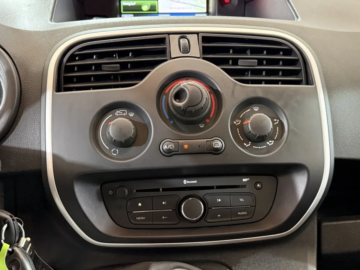 Vue rapprochée du tableau de bord noir du Renault Kangoo blanc 2021, montrant les commandes de climatisation et audio.