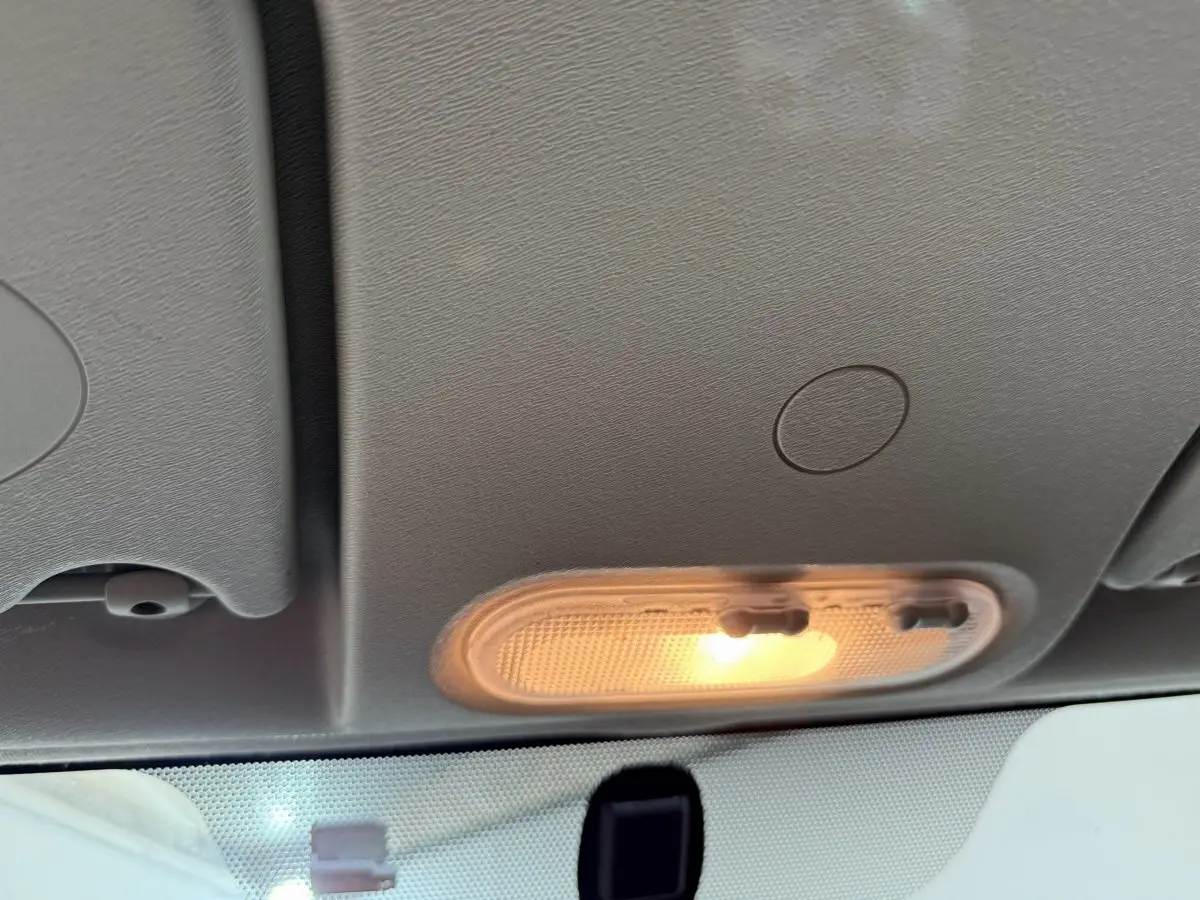 Plafonnier avant allumé vu de l'intérieur d'un Renault Kangoo blanc, avec toit clair et pare-brise partiel visible.