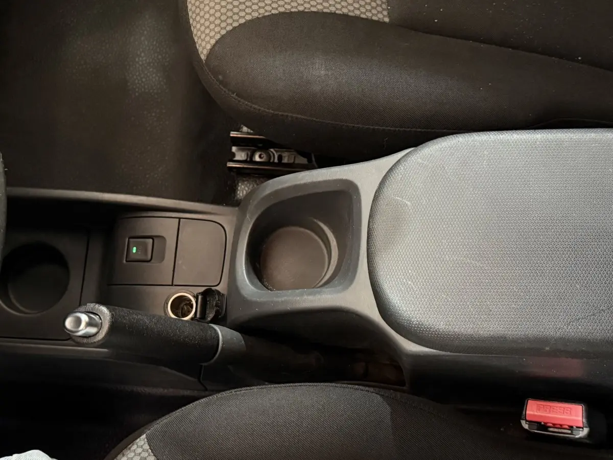 Vue intérieure centrée sur la console centrale noire avec frein à main et accoudoir entre sièges tissu gris et noir.