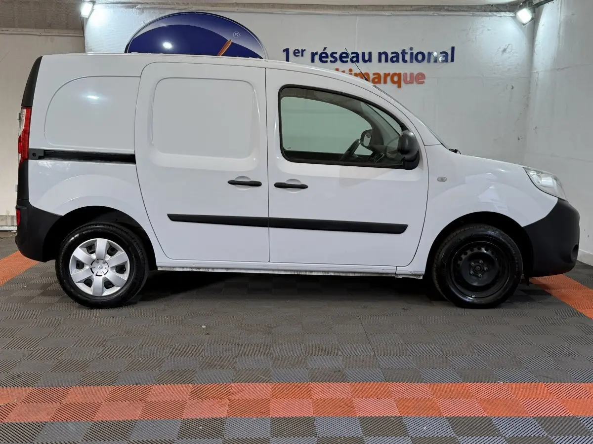 Profil droit d’un Renault Kangoo blanc utilitaire avec portes latérales pleines et jantes acier, en intérieur showroom.