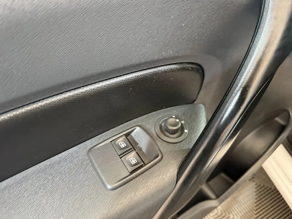 Gros plan sur les commandes de lève-vitres et réglage des rétroviseurs côté conducteur d’une Renault Kangoo blanche.