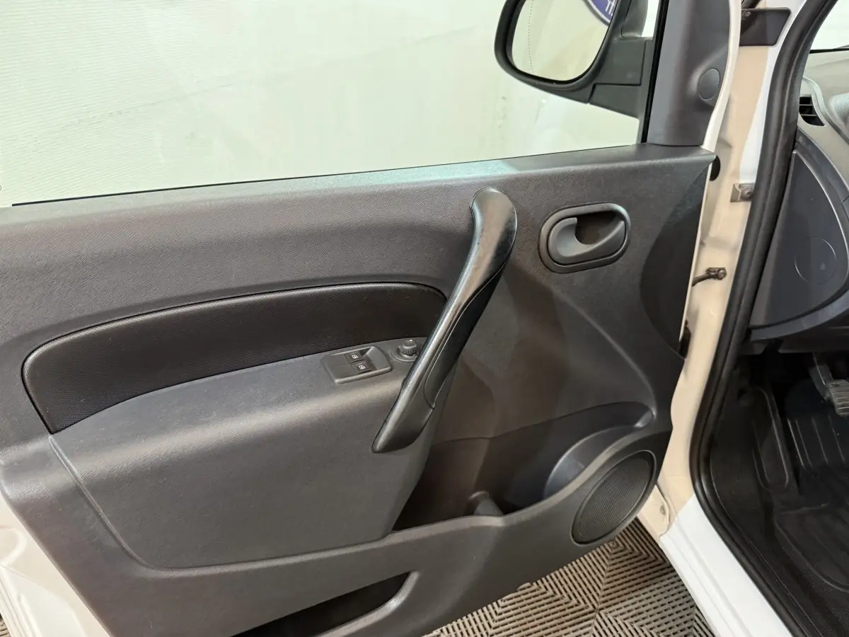 Vue intérieure côté gauche de la porte avant d’un Renault Kangoo blanc avec poignée noire et commandes de vitres électriques.