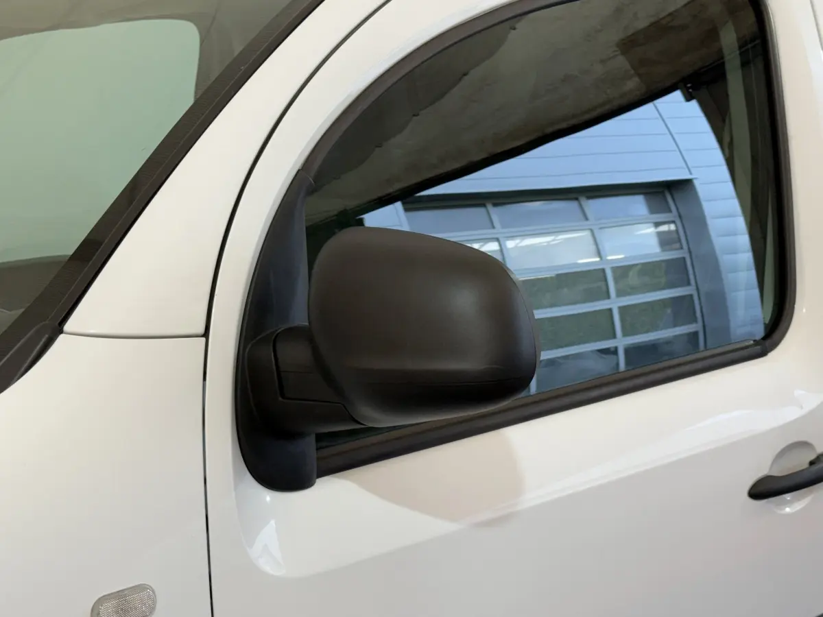 Gros plan sur le rétroviseur noir côté conducteur du Renault Kangoo blanc, avec la porte avant visible en arrière-plan.