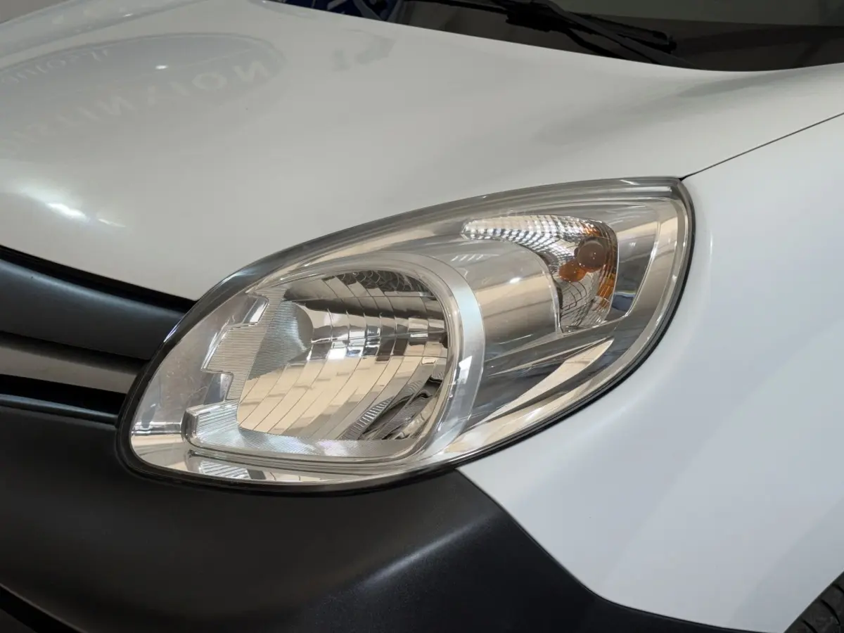 Gros plan sur le phare avant droit du Renault Kangoo blanc, soulignant le contour clair et la calandre noire adjacente.