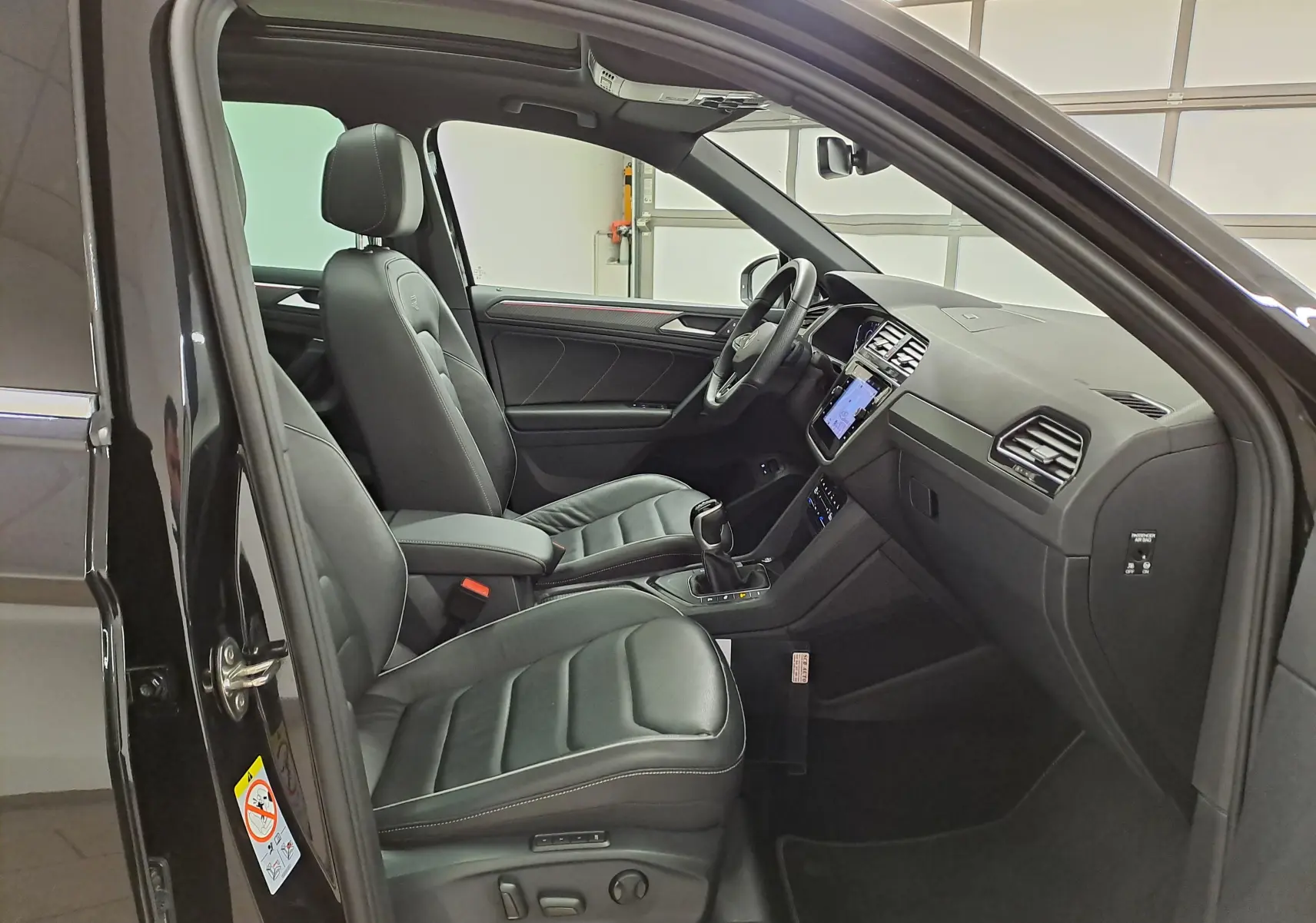 Vue intérieure côté conducteur du Volkswagen Tiguan 1.4 eHybrid 2023 avec sièges cuir noirs et tableau de bord moderne.