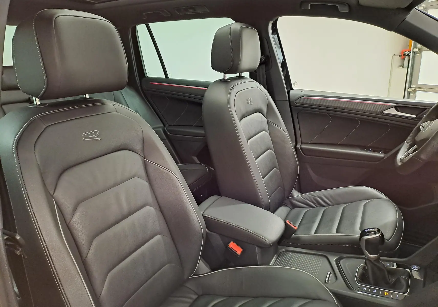 Vue intérieure côté droit du Volkswagen Tiguan 1.4 eHybrid 2023, sièges cuir noirs avec surpiqûres blanches et logo R brodé.