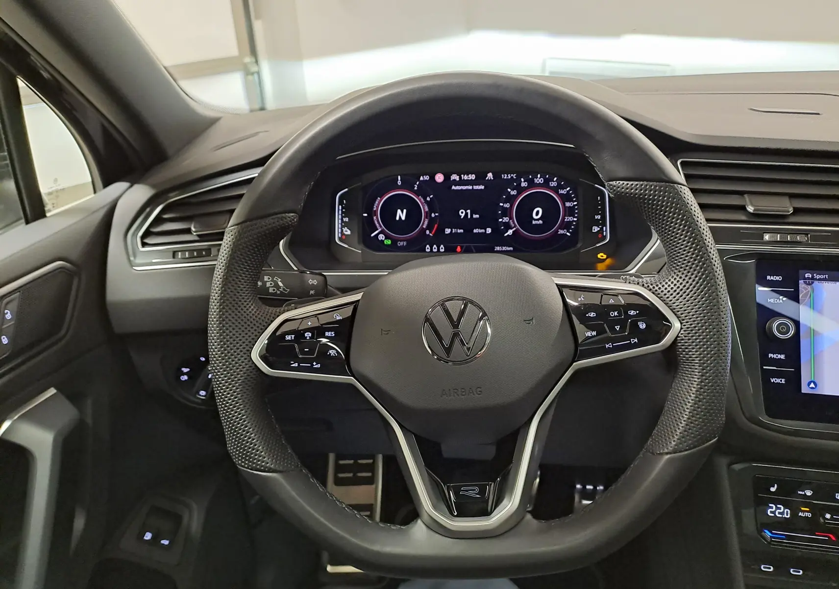 Vue intérieure centrée sur le volant multifonction du Volkswagen Tiguan 1.4 eHybrid noir avec tableau de bord numérique.