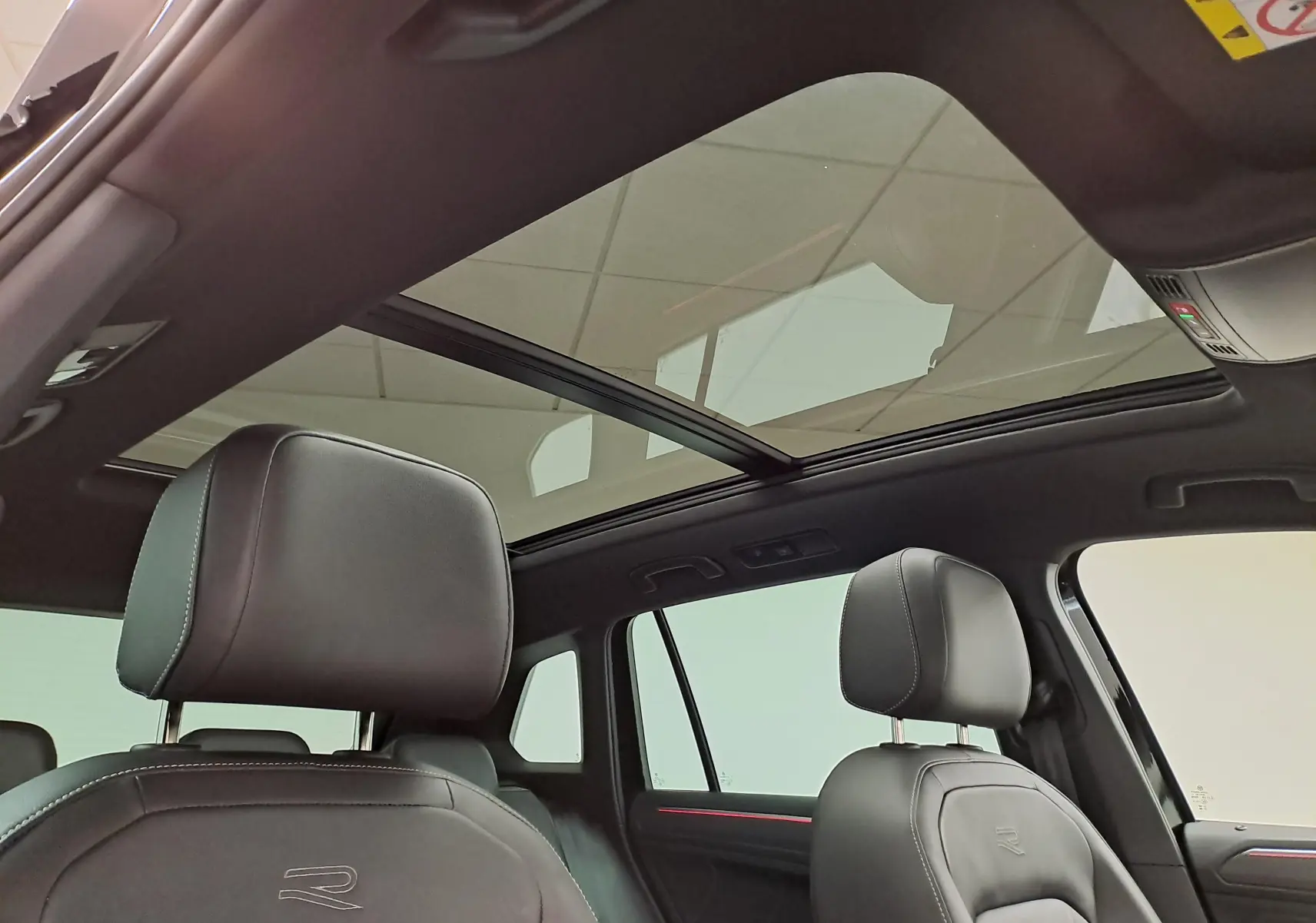 Vue intérieure du Volkswagen Tiguan 1.4 eHybrid 2023, toit panoramique et sièges cuir noirs avec logo R brodé.