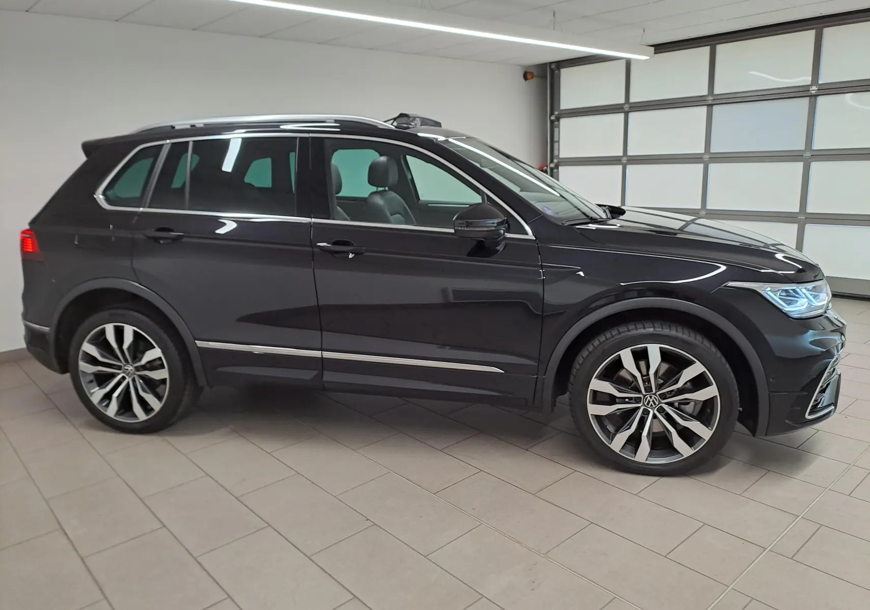 Vue de profil côté gauche d’un Volkswagen Tiguan 1.4 eHybrid noir intense nacré avec jantes 20 pouces Suzuka et attelage escamotable.