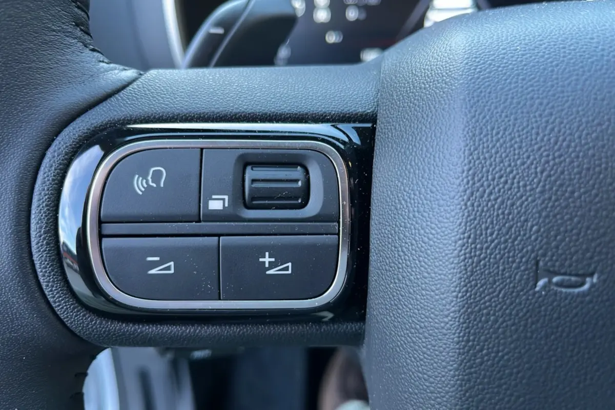 Gros plan sur les commandes vocales et de volume à gauche du volant cuir du Citroën C5 Aircross Hybrid blanc 2025.