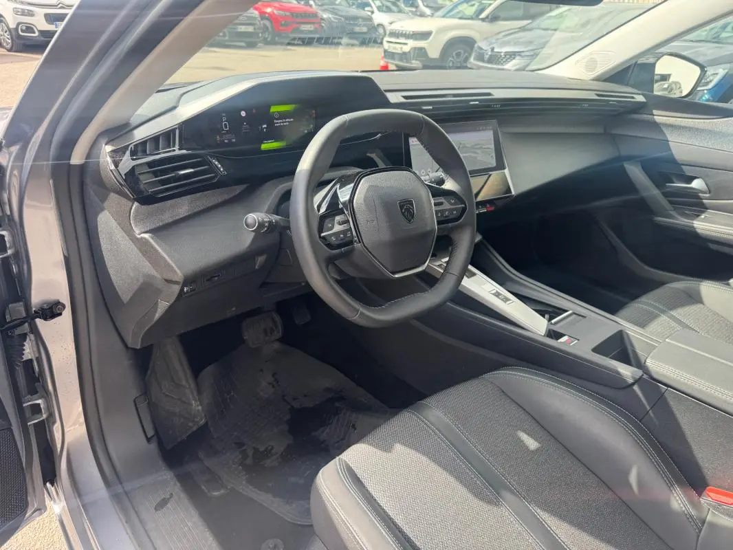Vue intérieure côté conducteur de la Peugeot 308 Hybrid gris 2025, avec volant compact et cockpit numérique lumineux.