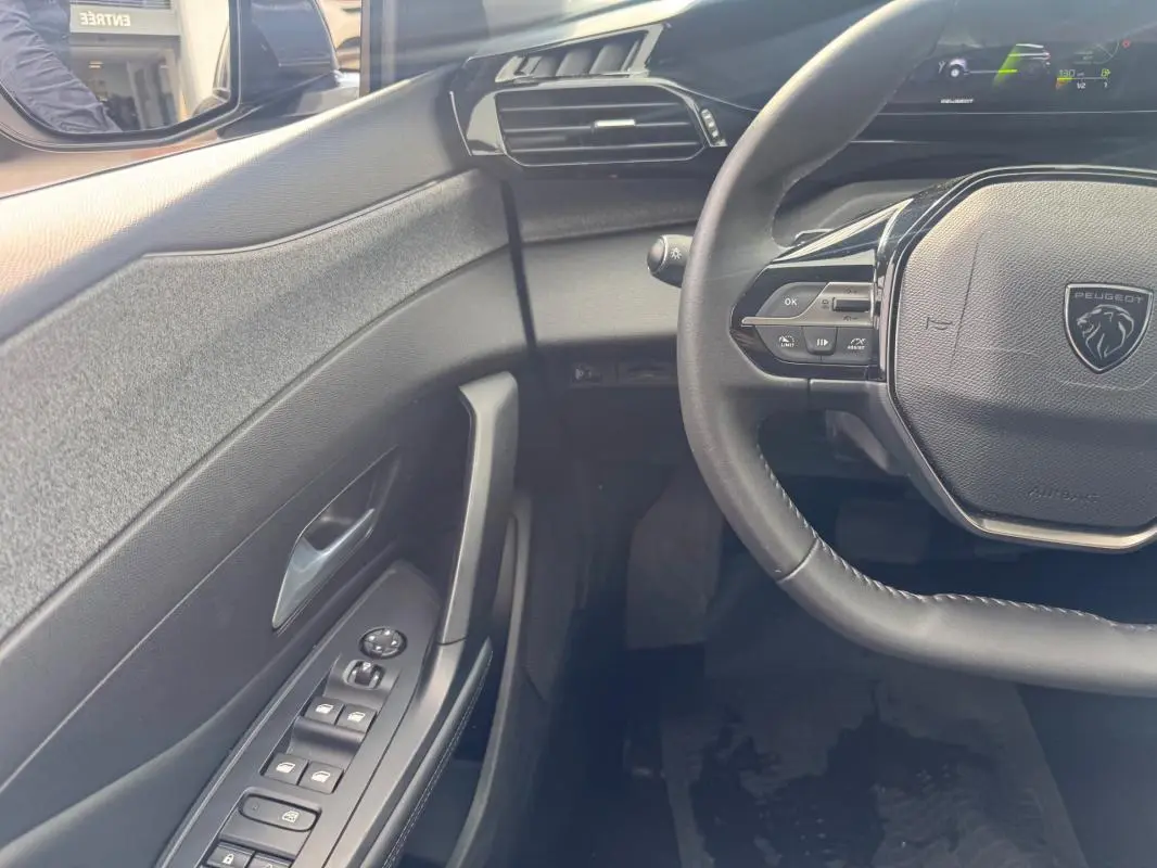 Vue intérieure côté conducteur de la Peugeot 308 gris, volant multifonction et commandes des vitres électriques visibles.