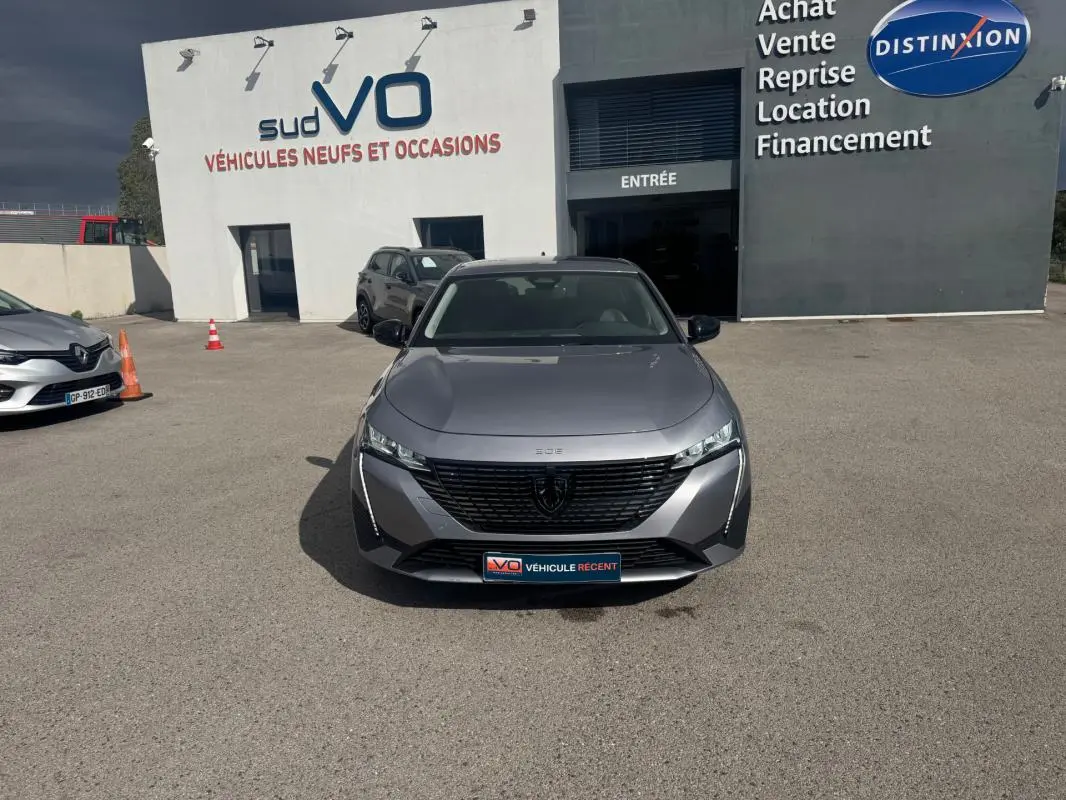 Vue frontale d'une Peugeot 308 Hybrid 145 gris métallisé, avec calandre noire et phares LED fins.