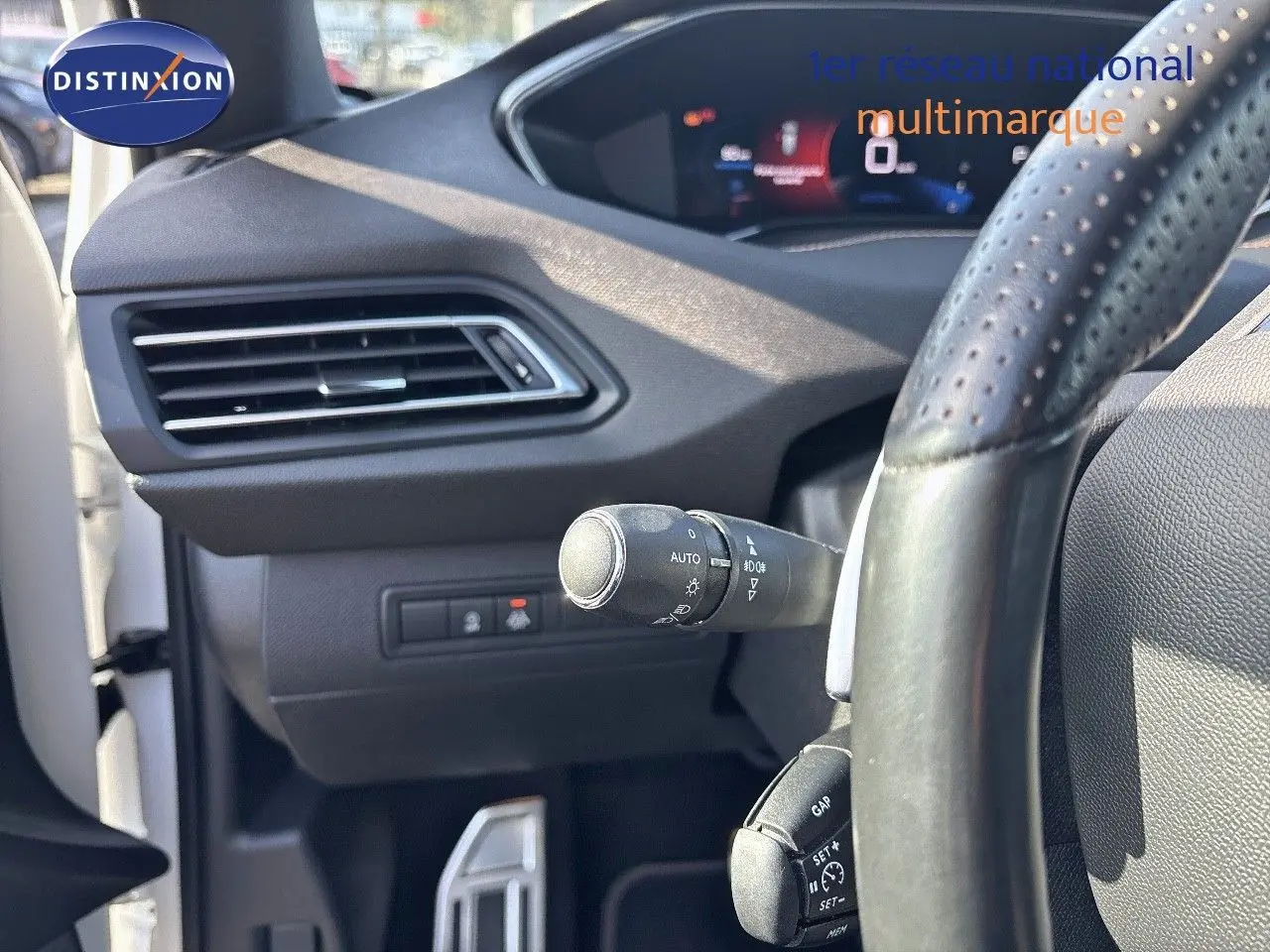 Gros plan sur la partie gauche du tableau de bord et volant perforé d'une Peugeot 308 blanc nacré de 2021.