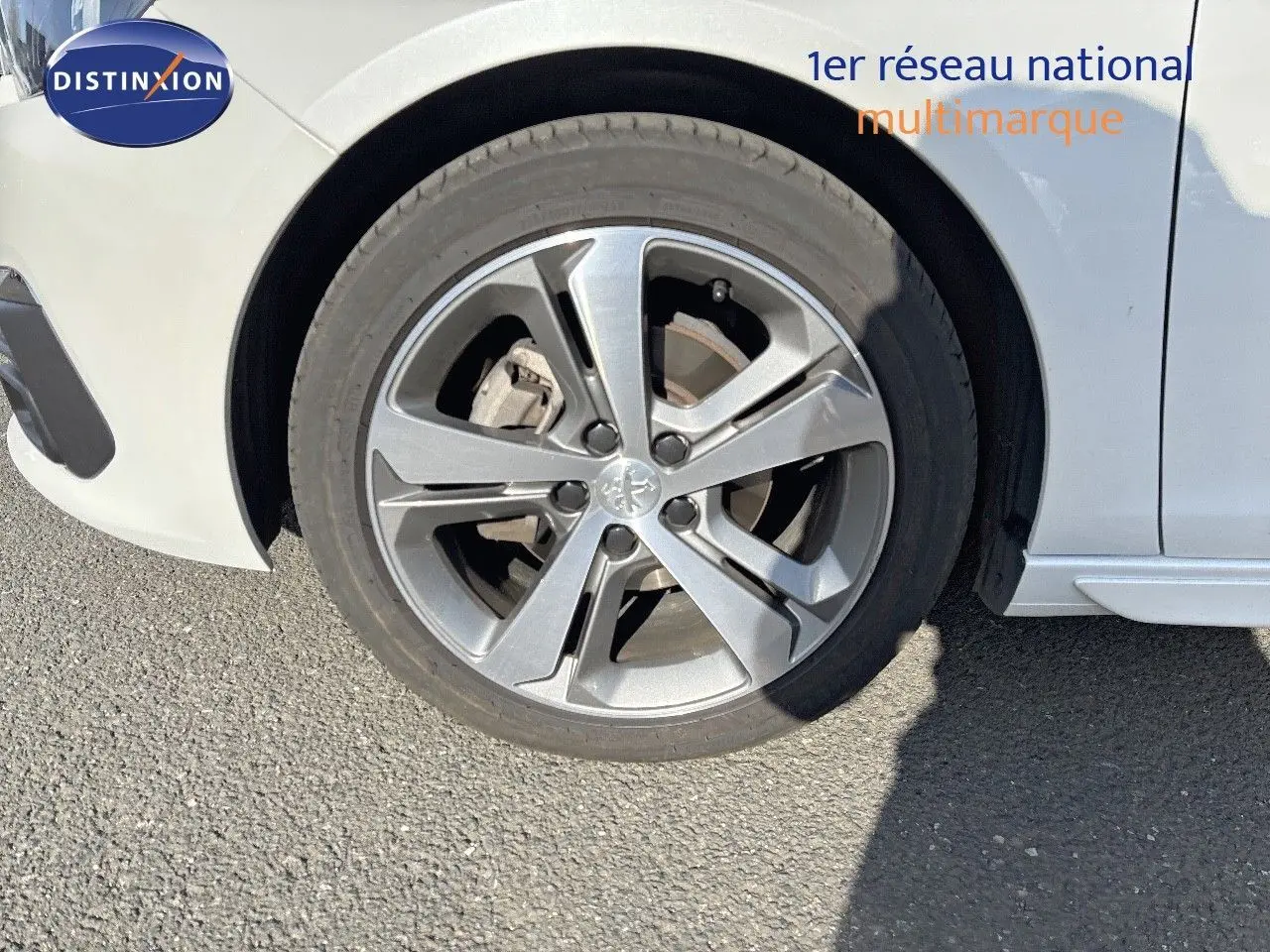 Gros plan sur la roue avant gauche d'une Peugeot 308 blanc nacré, mettant en valeur la jante alliage moderne.