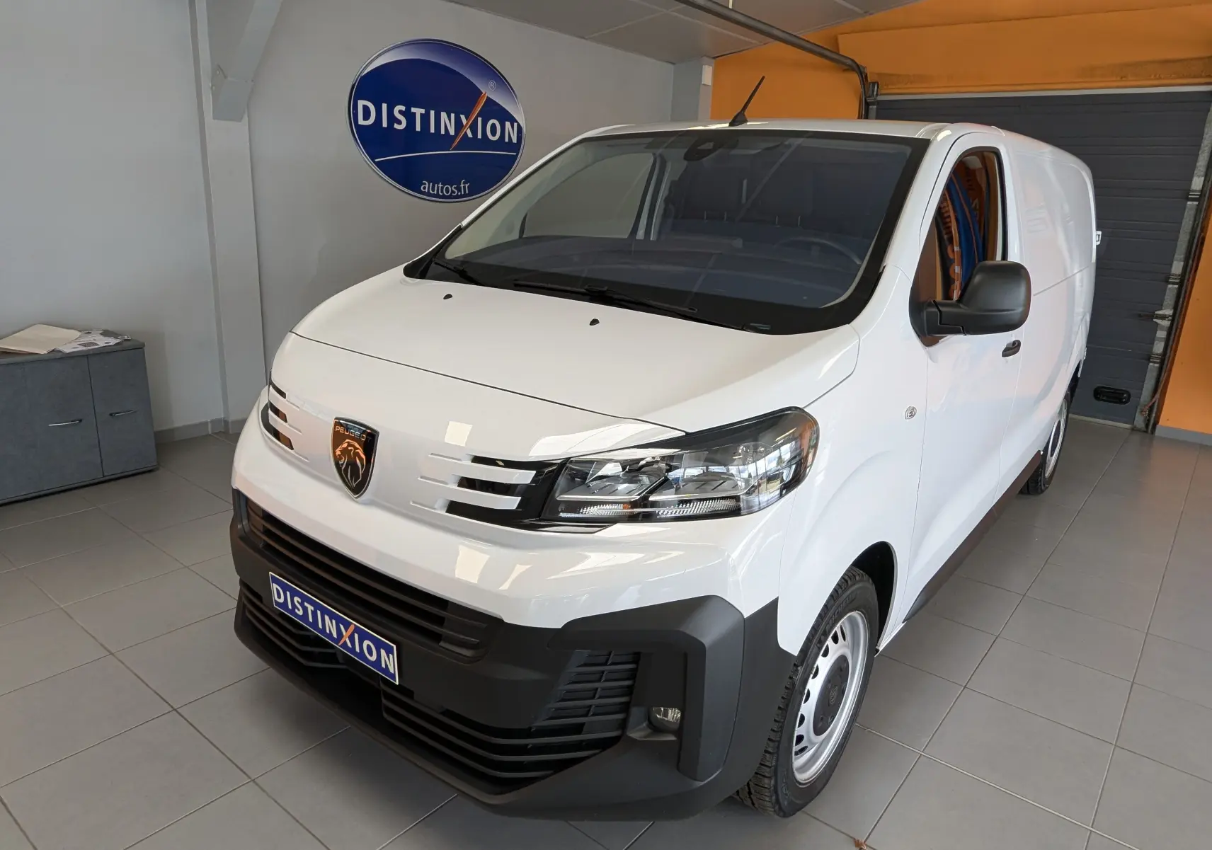 Peugeot Expert Fourgon blanc en 3/4 avant droit, avec calandre noire et jantes tôles 17 pouces visibles en intérieur showroom.