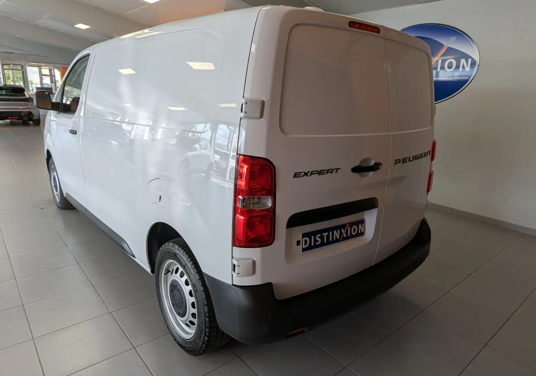 Vue 3/4 arrière droite du Peugeot Expert Fourgon blanc 2024 avec jantes tôles et portes arrière fermées en intérieur showroom.