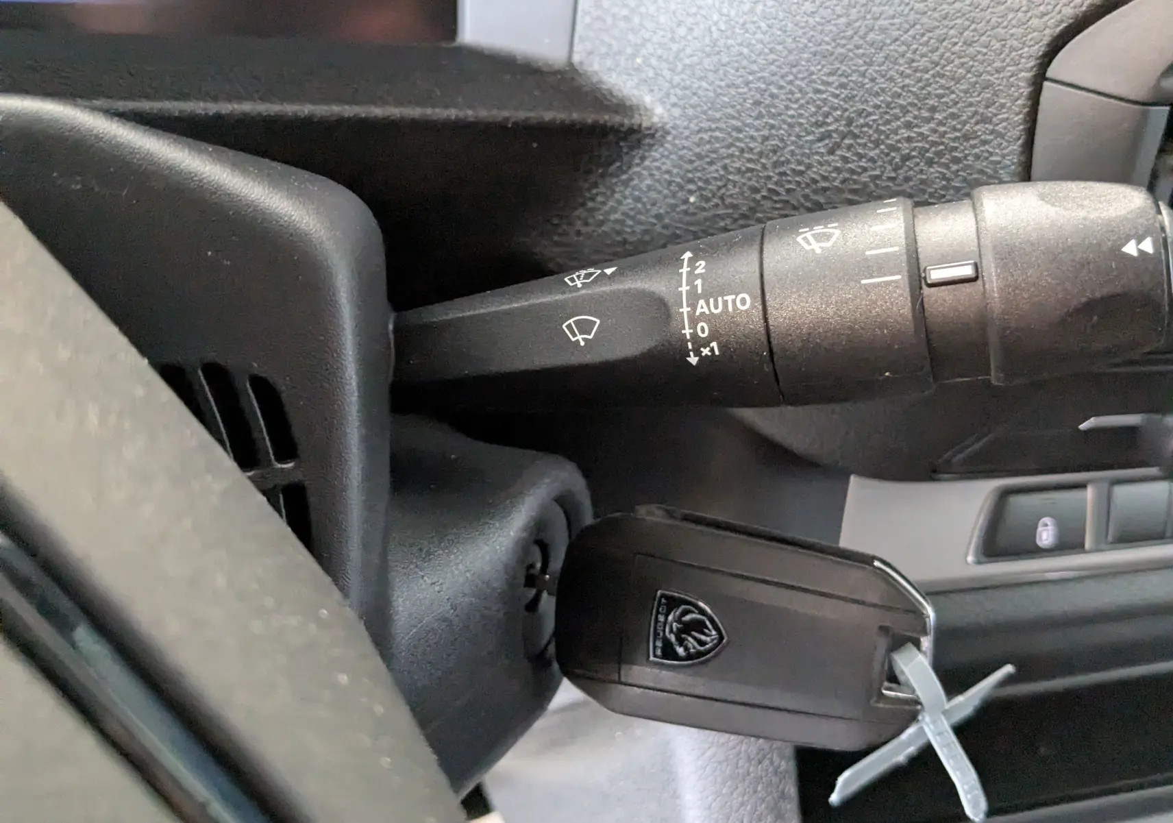 Gros plan sur la commande d’essuie-glace et la clé de contact du Peugeot Expert Fourgon blanc, tableau de bord partiel visible.