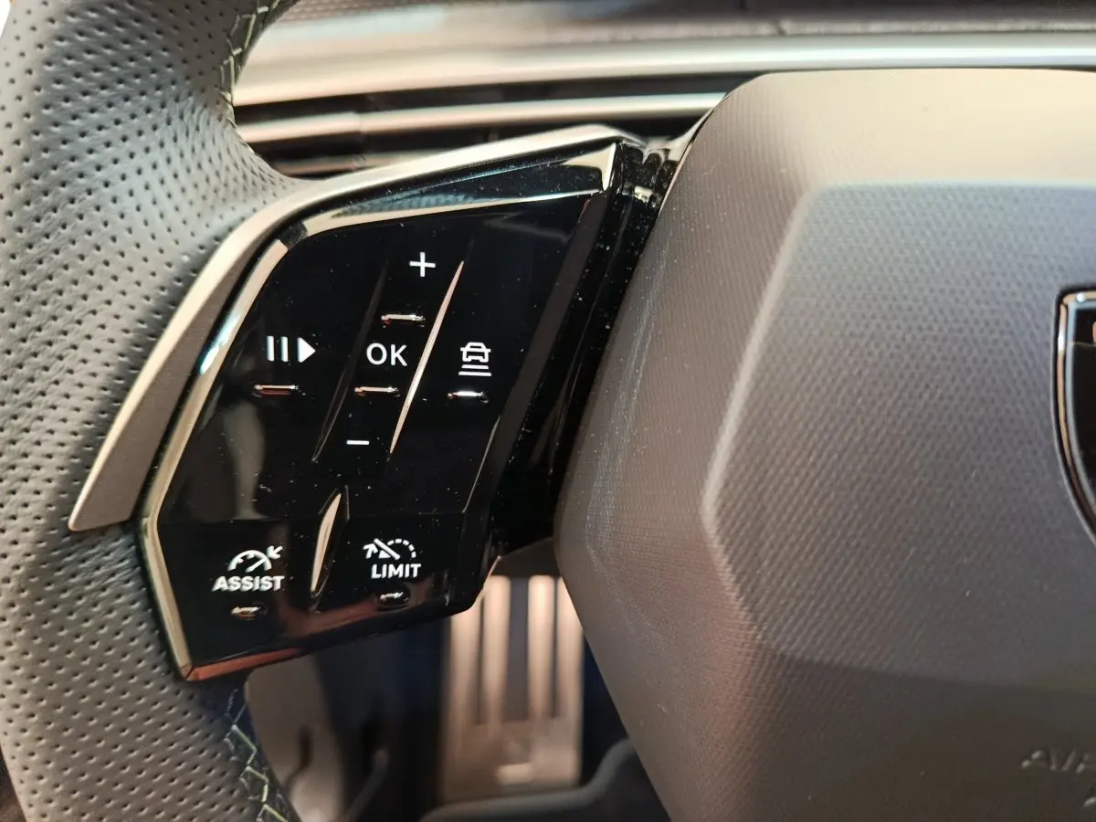 Gros plan sur les commandes noires multifonctions à gauche du volant perforé du Peugeot 3008 gris clair 2025.