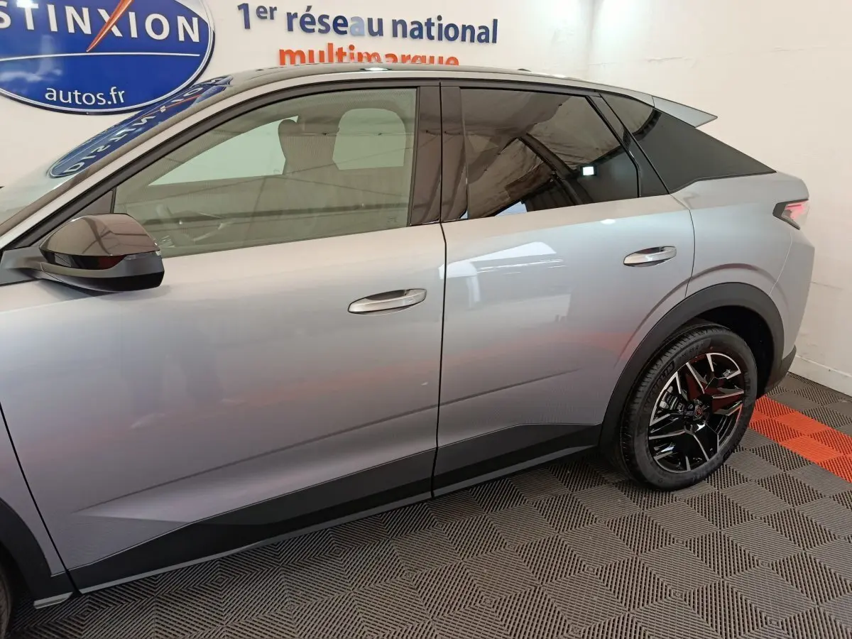 Profil côté gauche du Peugeot 3008 gris clair 2025 avec jantes noires et vitres teintées dans un showroom.