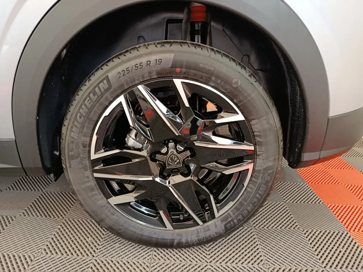 Gros plan sur la roue avant droite du Peugeot 3008 gris clair 1.2 HYBRID 145 E-DCS6 GT avec jante noire et chromée.