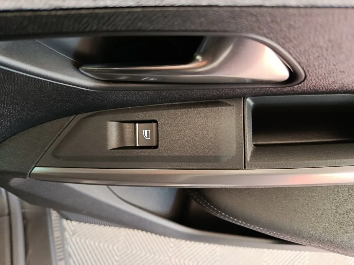 Gros plan sur la poignée intérieure et le bouton de lève-vitre côté gauche du Peugeot 3008 gris clair.