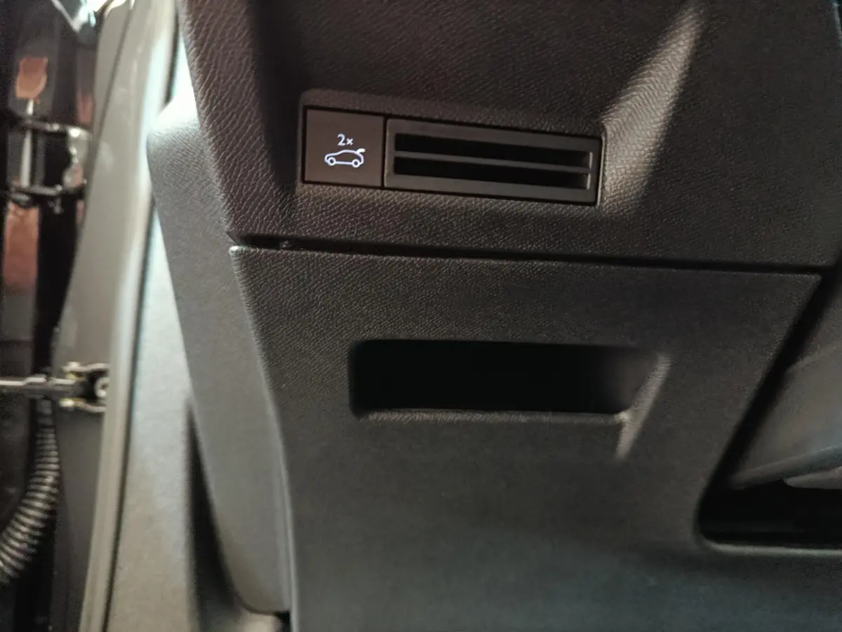 Détail du bouton d'ouverture électrique du coffre sur la partie inférieure du tableau de bord du Peugeot 3008 gris clair.