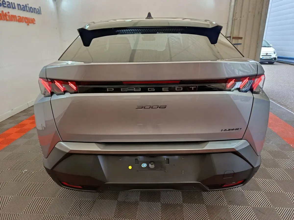 Vue arrière d'un Peugeot 3008 gris clair hybride 2025 avec feux LED caractéristiques et logo central lumineux.