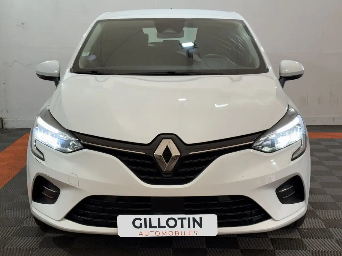 Vue frontale d'une Renault Clio Business blanche de 2021 avec phares LED allumés et calandre noire distinctive.