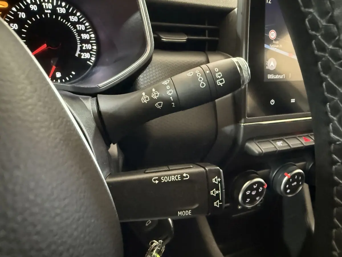 Gros plan sur le volant et la commande des essuie-glaces d’une Renault Clio Business blanche, avec écran tactile et commandes de climatisation.