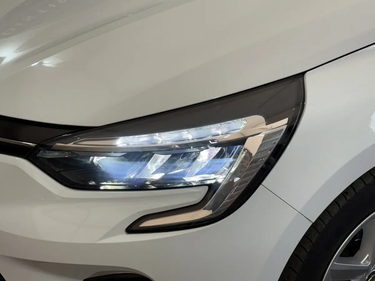 Gros plan sur le phare avant droit blanc d'une Renault Clio Business 2021, mettant en valeur les LED et la carrosserie lisse.