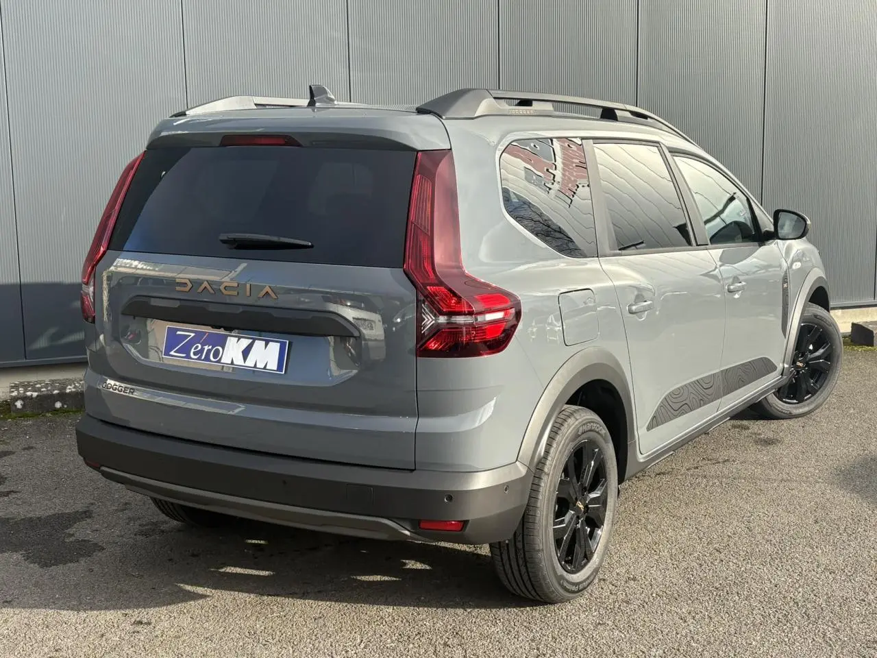 Vue 3/4 arrière droite du Dacia Jogger Gris Urbain avec jantes noires et barres de toit modulaires.