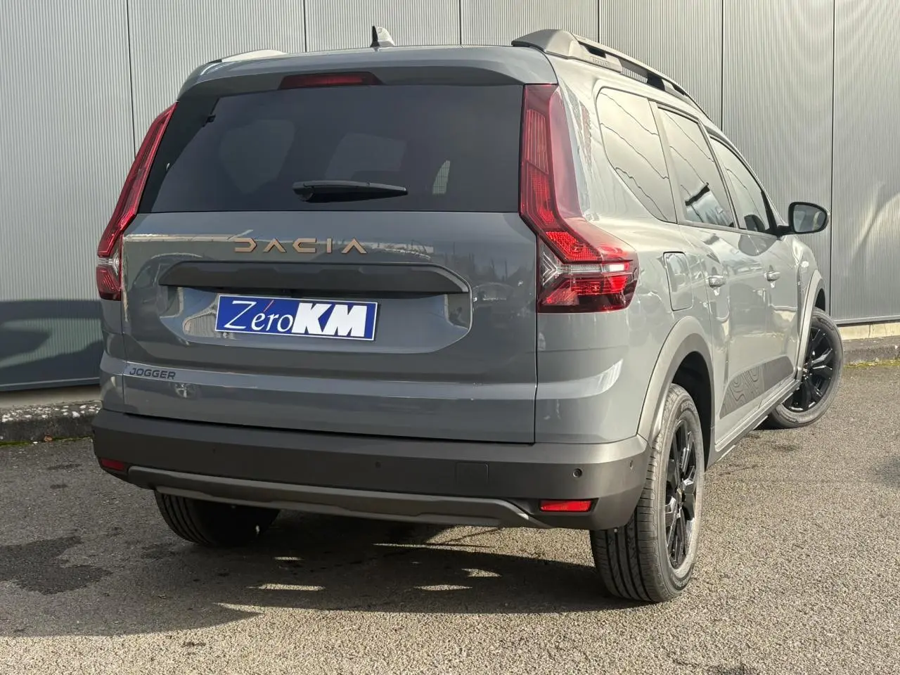 Vue 3/4 arrière droite d'un Dacia Jogger Gris Urbain avec jantes noires et barres de toit longitudinales.