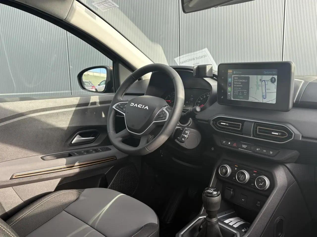 Intérieur côté conducteur du Dacia Jogger 2024 avec volant, écran tactile GPS et levier de vitesse manuel visibles.