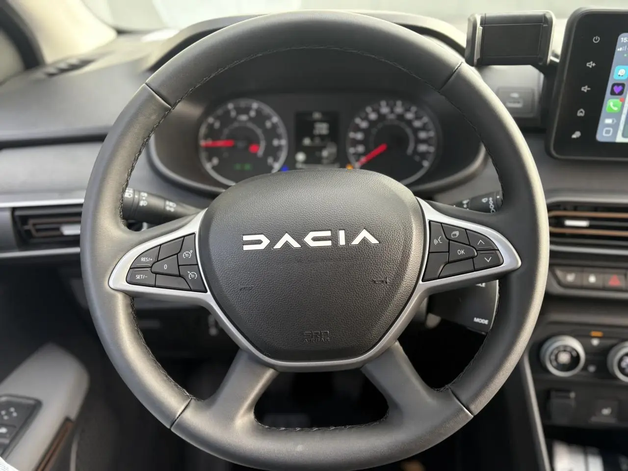 Vue rapprochée du volant noir du Dacia Jogger 2024 avec commandes intégrées et tableau de bord en arrière-plan.