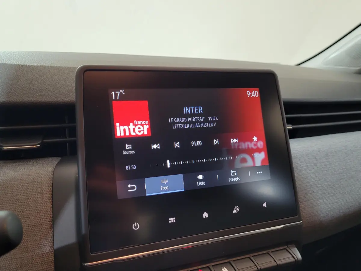 Écran tactile central affichant la radio France Inter dans l'habitacle clair d'une Renault Clio bleu, vue de face.