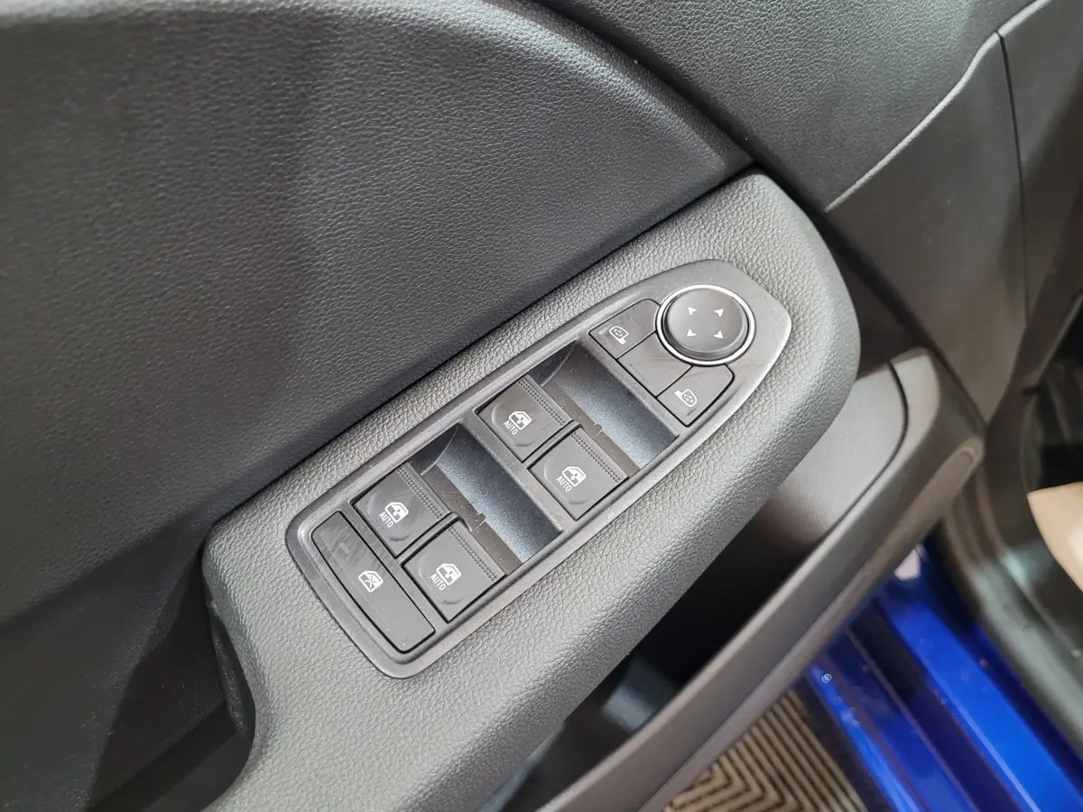 Gros plan sur les commandes des vitres et rétroviseurs sur la porte côté conducteur d'une Renault Clio bleu 2025.