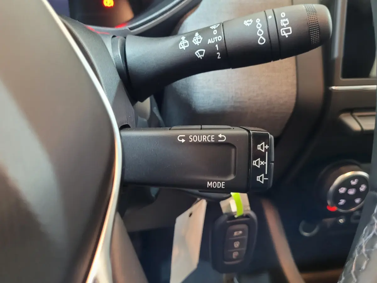Gros plan sur les commandes au volant de la Renault Clio bleu, montrant les boutons source et mode audio.