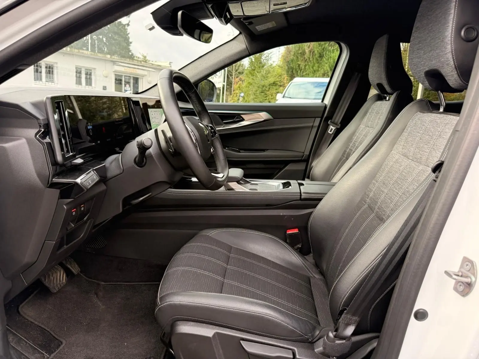 Vue intérieure côté conducteur du Renault Austral E-Tech 200 blanc nacré, sièges tissu et cuir noir avec tableau de bord moderne.