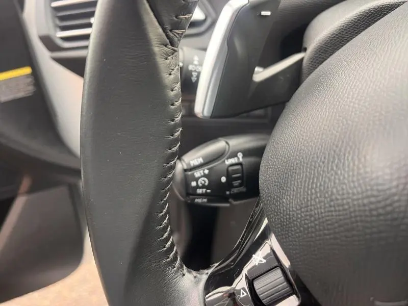 Gros plan sur le volant cuir noir et la commande multifonction de la Peugeot 308 Blanc Banquise, intérieur avant.