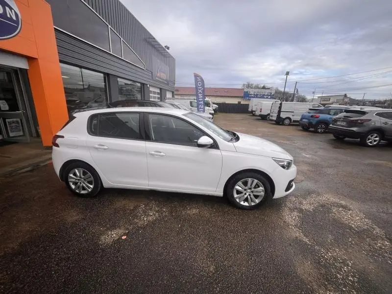 Peugeot 308 blanc banquise vue de profil côté gauche, stationnée devant un bâtiment commercial.