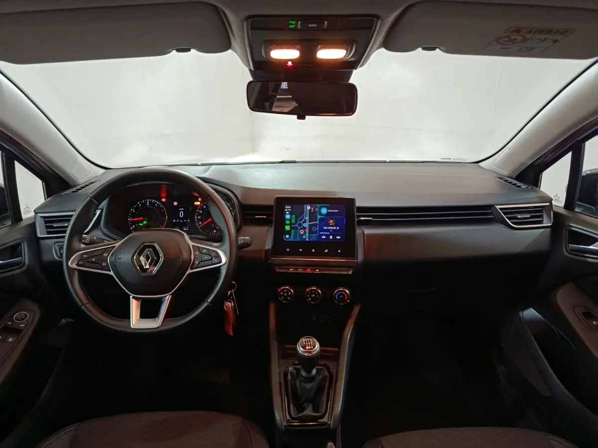 Vue intérieure avant de la Renault Clio gris clair 2023, volant multifonctions cuir et écran tactile central allumé.