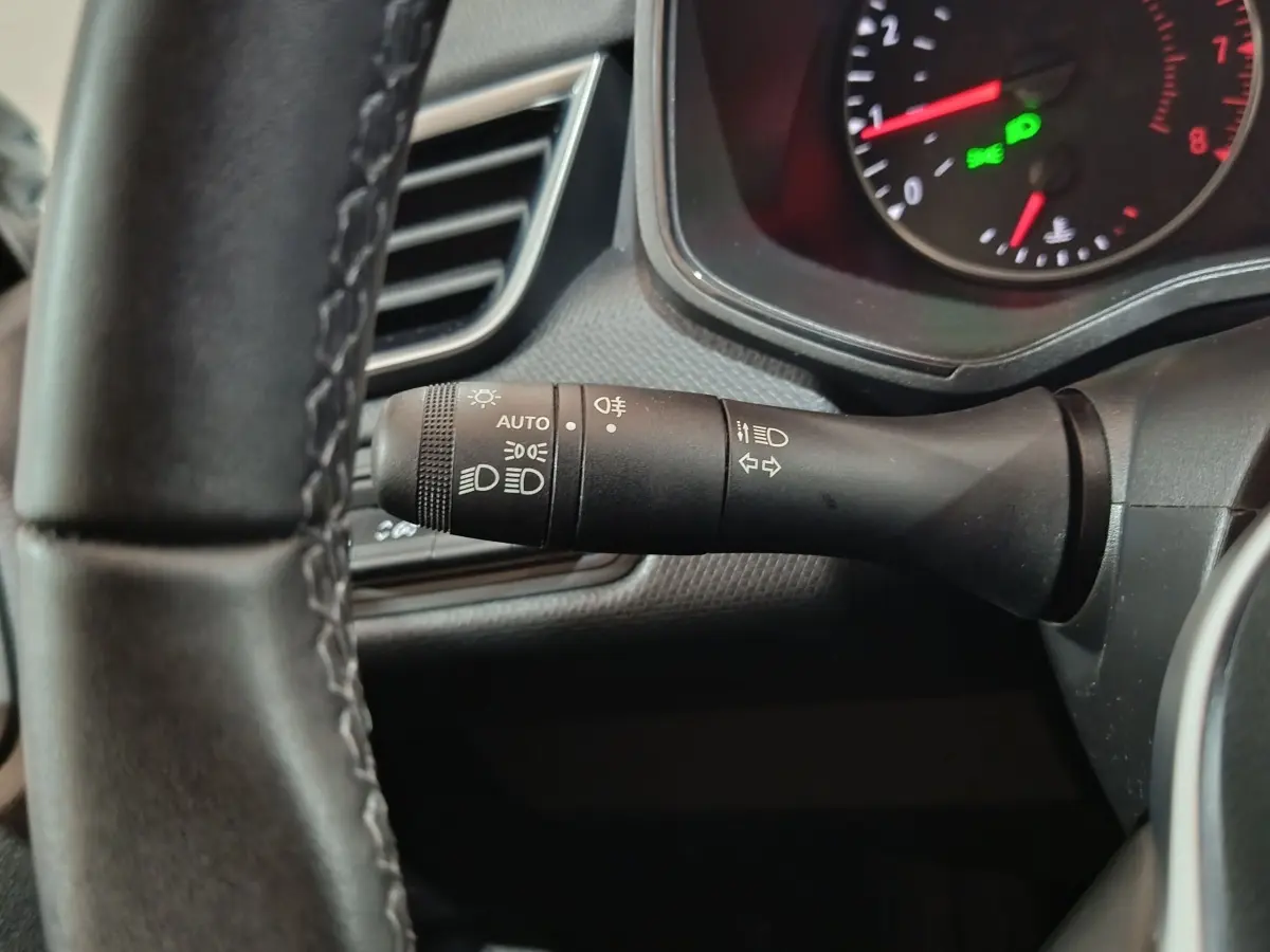 Gros plan sur la manette des phares et clignotants à gauche du volant cuir synthétique d’une Renault Clio gris clair 2023.