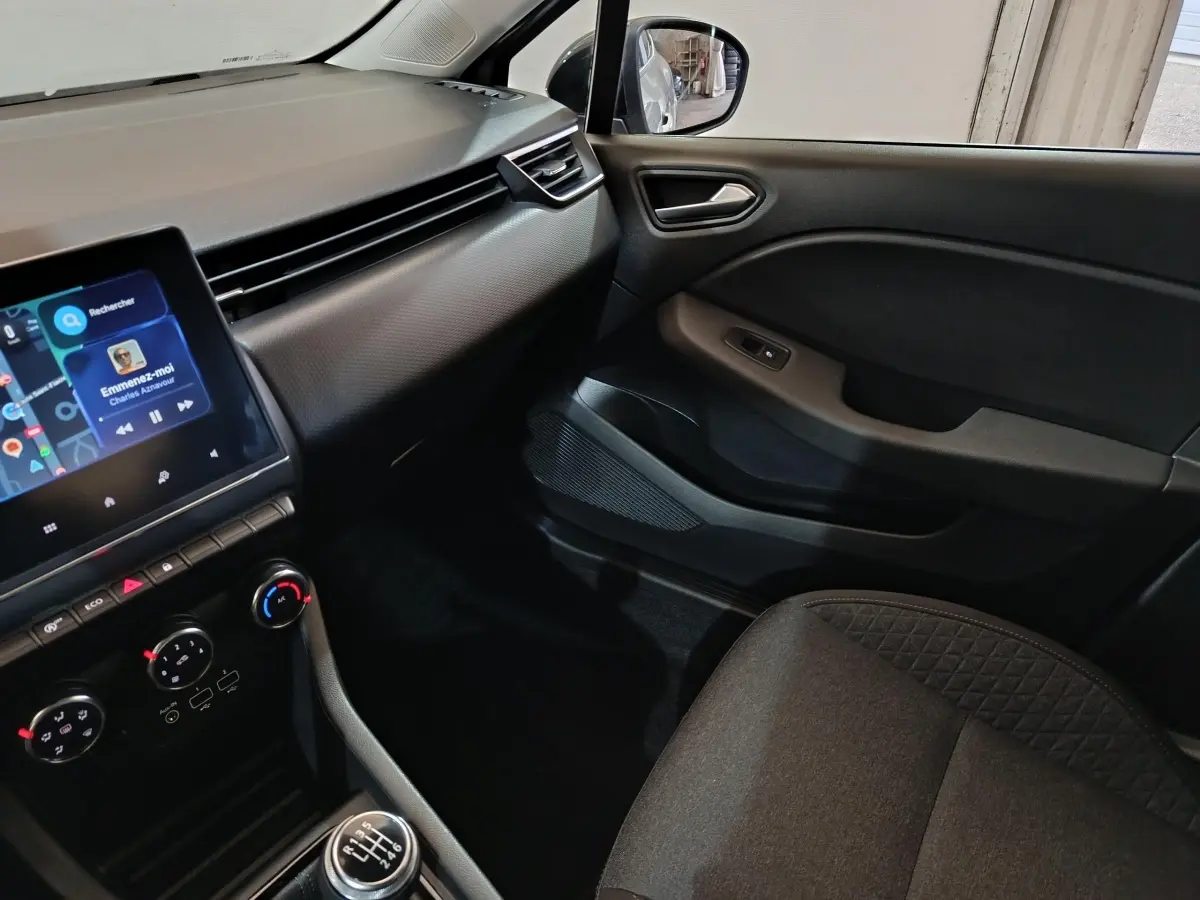 Vue intérieure côté passager de la Renault Clio 2023 gris clair, avec tableau de bord et écran tactile central.
