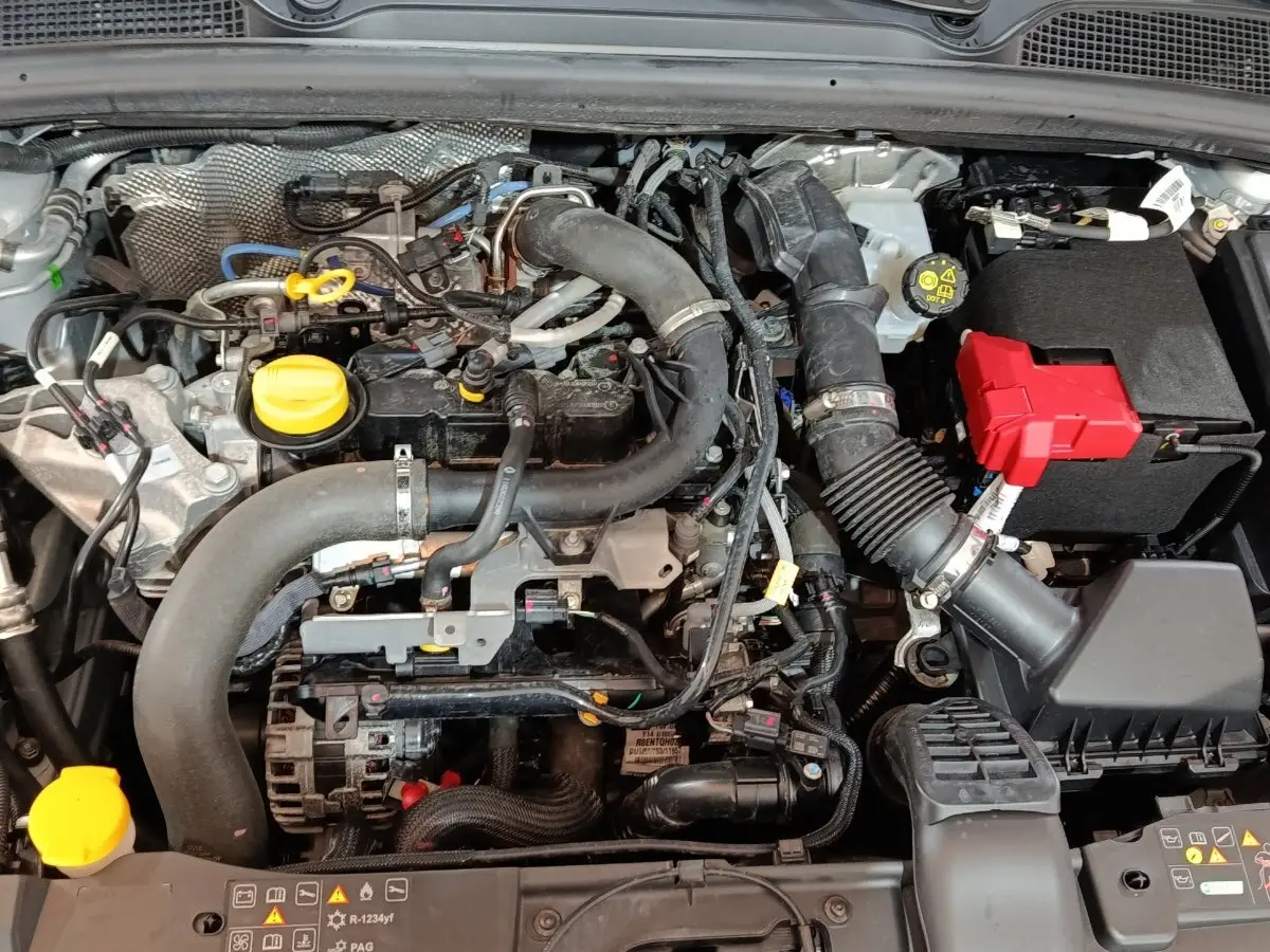 Vue rapprochée du moteur essence gris clair de la Renault Clio 2023 avec éléments jaunes et boîte à fusibles rouge visible.