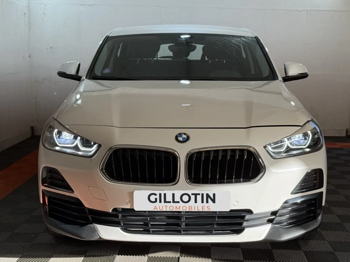 BMW X2 sDrive18i Lounge blanc vue de face avec phares LED allumés dans un garage fermé.