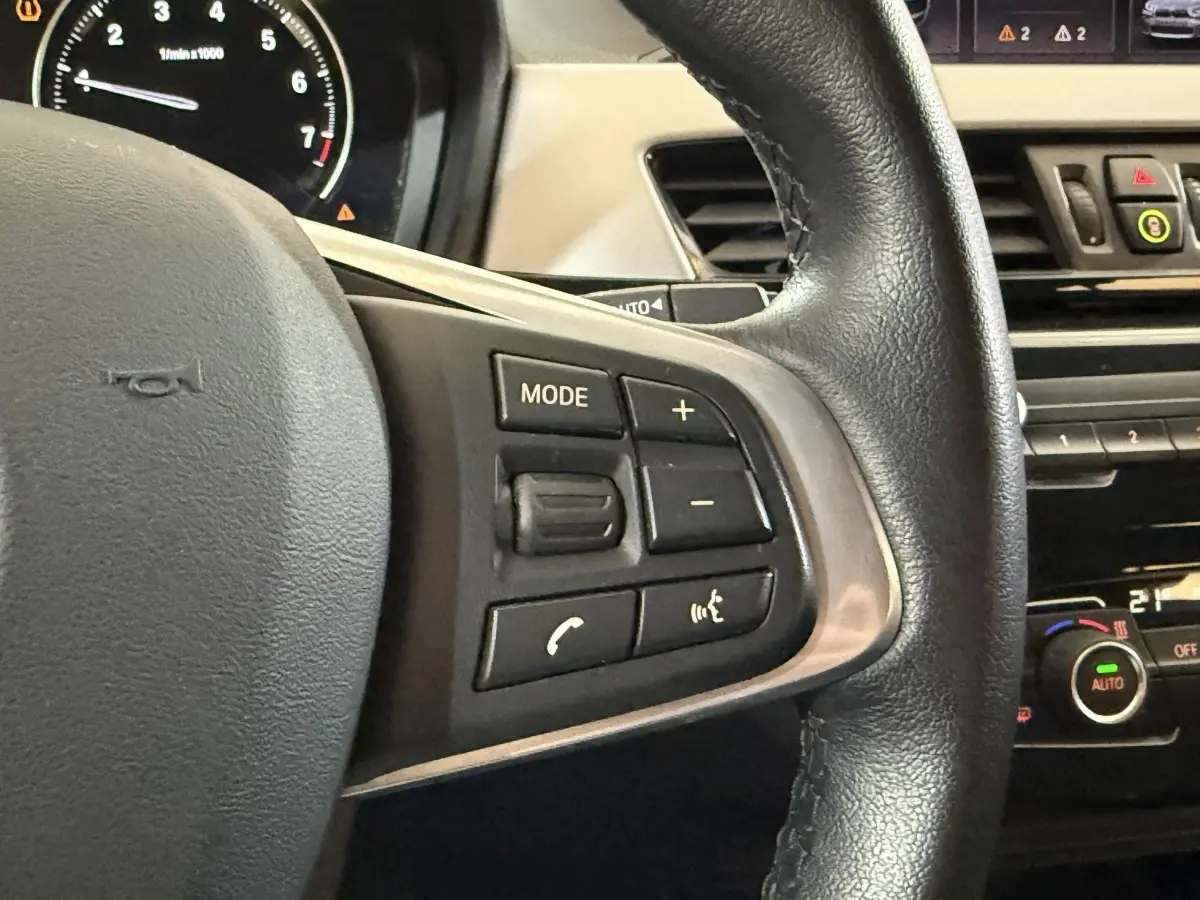 Gros plan sur le volant cuir noir de la BMW X2 sDrive18i Lounge 2023 avec commandes multifonctions visibles.