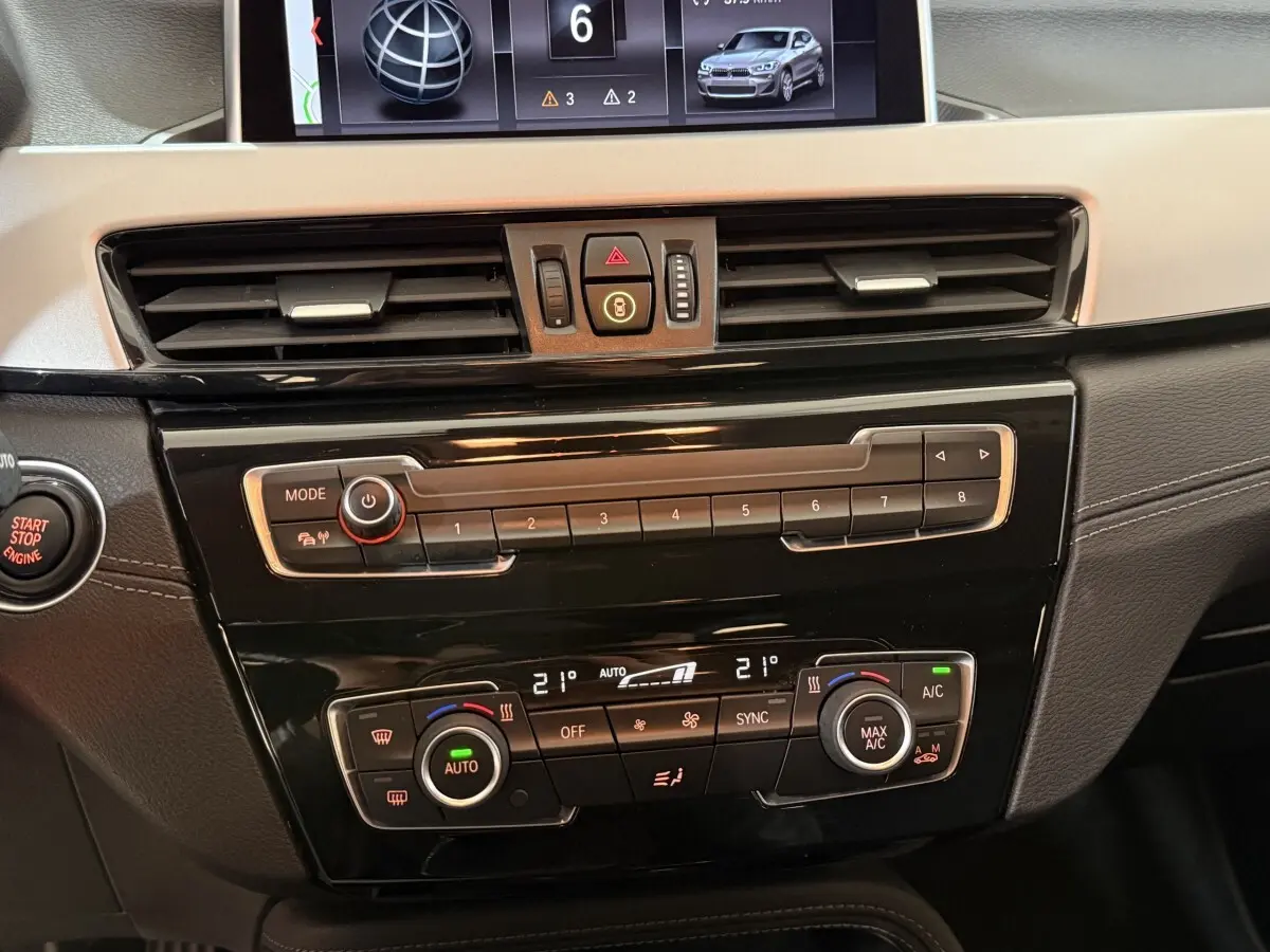 Vue rapprochée du tableau de bord noir et beige du BMW X2 sDrive18i Lounge 2023 avec commandes climatisation et écran central.